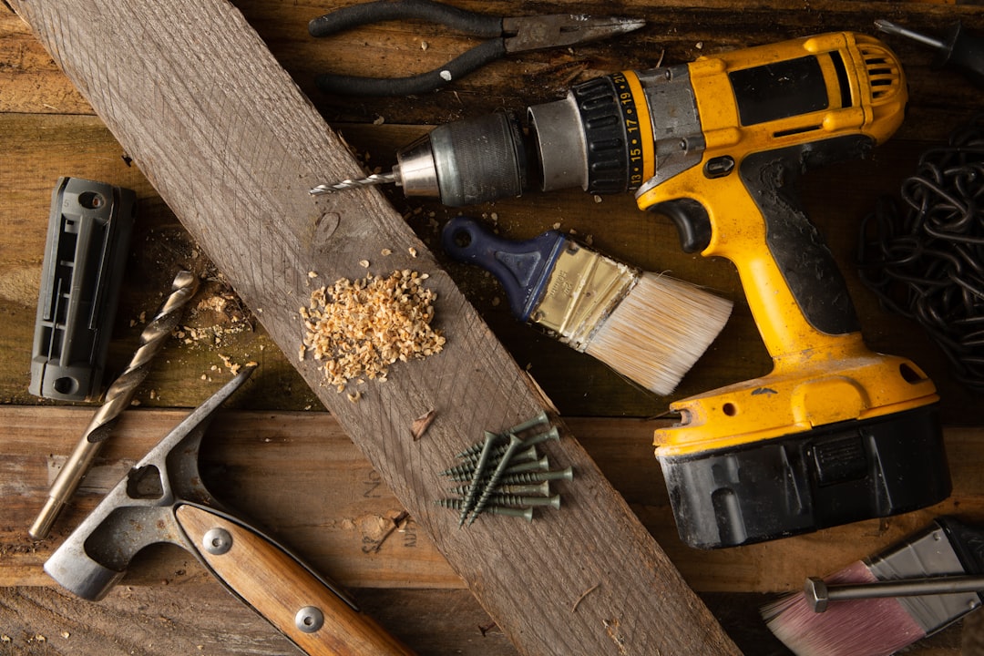 about-img A variety of tools, including a hammer and cordless drill, sit on top of a table made of wood boards.